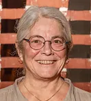 Portræt af en smilende kvinde med gråt hår og briller.