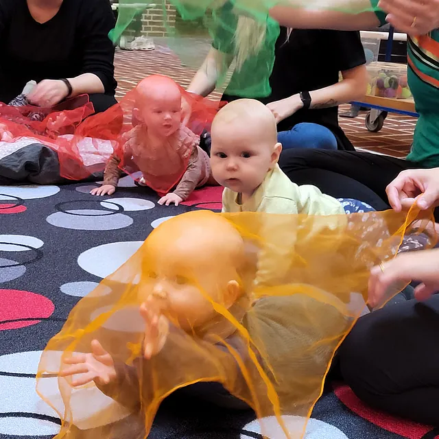 Babyer leger med farverige tørklæder på et mønstret tæppe.