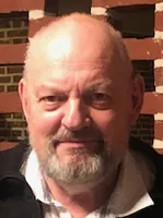 Portræt af en skaldet mand med skæg og briller.