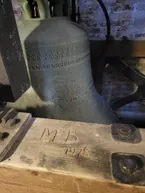 En kirkeklokke med dansk inskription og en træbjælke.