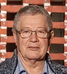 Portræt af en alvorligt udseende mand med gråt hår og en ternet skjorte.