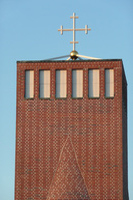 Toppen af et moderne kirketårn i mursten med et kors.