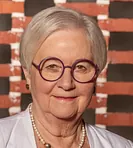 Portræt af en smilende kvinde med en perlekæde og briller.