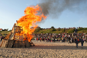 Et stort bål på en strand med tilskuere.