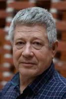 Portræt af en alvorligt udseende mand med gråt hår og en ternet skjorte.