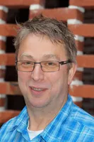 Portræt af en smilende mand med briller og en ternet skjorte.