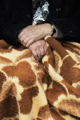 Ældre hænder, der er foldet over et tæppe.