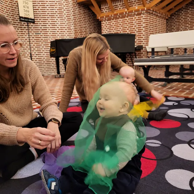 To kvinder og en baby leger med tørklæder på et tæppe.