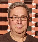 Portræt af en smilende mand med briller og en ternet skjorte.