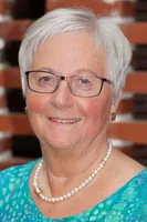 Portræt af en smilende kvinde med en perlekæde og briller.