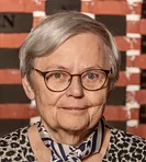 Portræt af en smilende kvinde med gråt hår og briller.