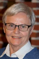 Portræt af en smilende kvinde med gråt hår og briller.