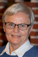 Portræt af en smilende kvinde med gråt hår og briller.