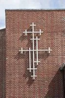 Et moderne kors af hvide rør på en murstenskirkemur.