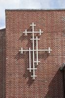 Et moderne kors af hvide rør på en murstenskirkemur.